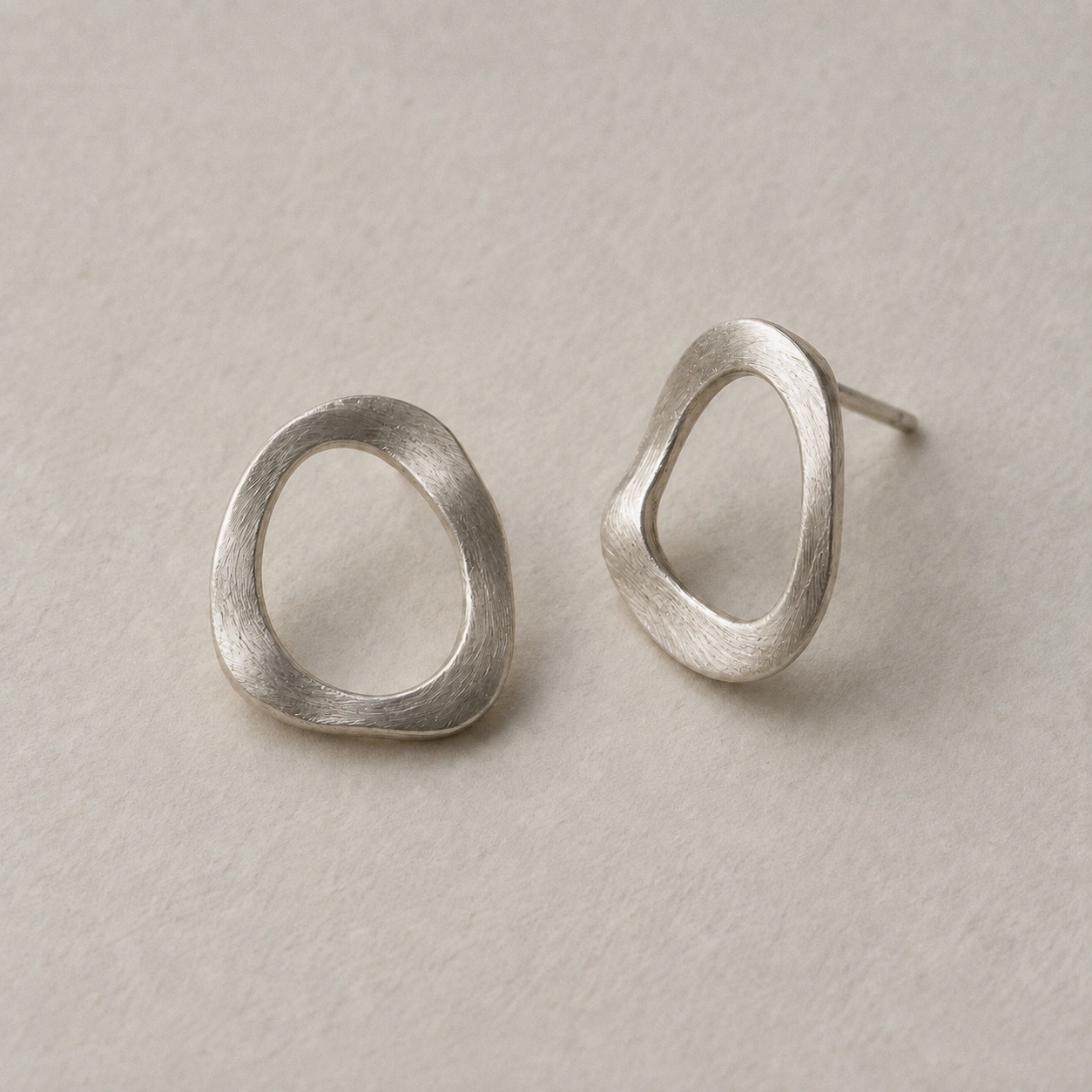 A pair of small, softly sculpted silver earrings on ivory paper.