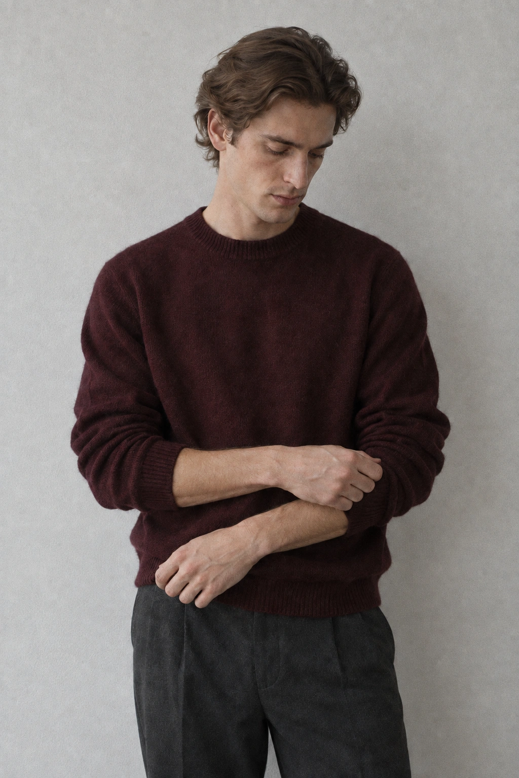 A medium photograph of a man looking down while adjusting the sleeve of a burgundy wool pullover.